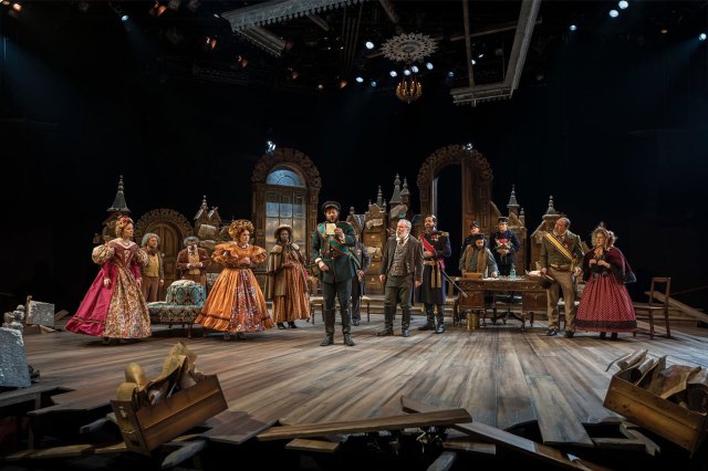 A cast of actors in 19th-century costumes on stage.